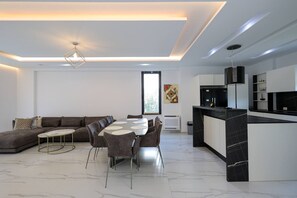 A modern living room with a dining area, a kitchen, and a large window. - Sanpietro Vacation Villa 009 (Ishëm)