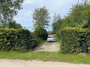 Ein Schotterweg führt zu einem weißen Auto, das vor einem Haus mit einem Metalltor geparkt ist.