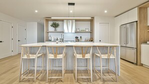 Eine moderne Küche mit Kochinsel, Barhocker, Edelstahlgeräten und einer Backspülle mit Fischgrätmuster.