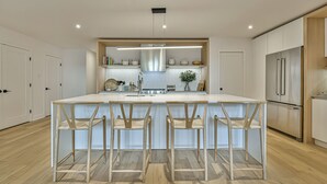 A modern kitchen with a central island, bar stools, a stainless steel refrigerator, and wooden cabinetry.