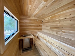 A wooden cabin interior with a window, a small table, and a bench. - La Maison Blanche | Hot Tub & Sauna | Pool Table, Fire Pit & Close to Resort (Mont-Tremblant)