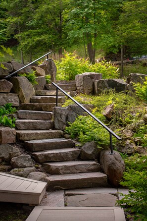 Un escalier en pierre, agrémenté de rampes métalliques, entouré de verdure et de rochers.
