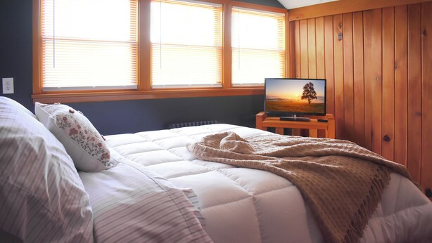 Een slaapkamer met een bed, een televisie op een standaard en een raam met zonwering.