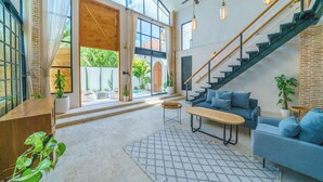 Ein großzügiger Wohnbereich mit Treppe, einem blauen Sofa, einem Holztisch und Blick auf einen Garten durch große Fenster.