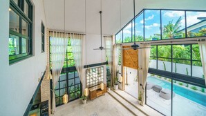 Ein geräumiges Zimmer mit großem Fenster mit Blick auf einen Pool, einer Holzbank und einem Deckenventilator.