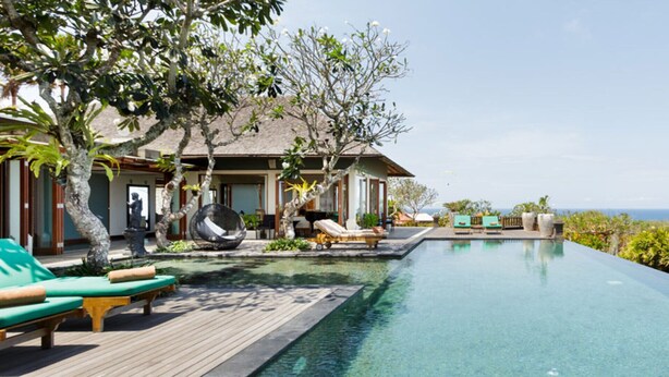 A resort with a clear infinity pool, lounge chairs, and a view of the ocean.
