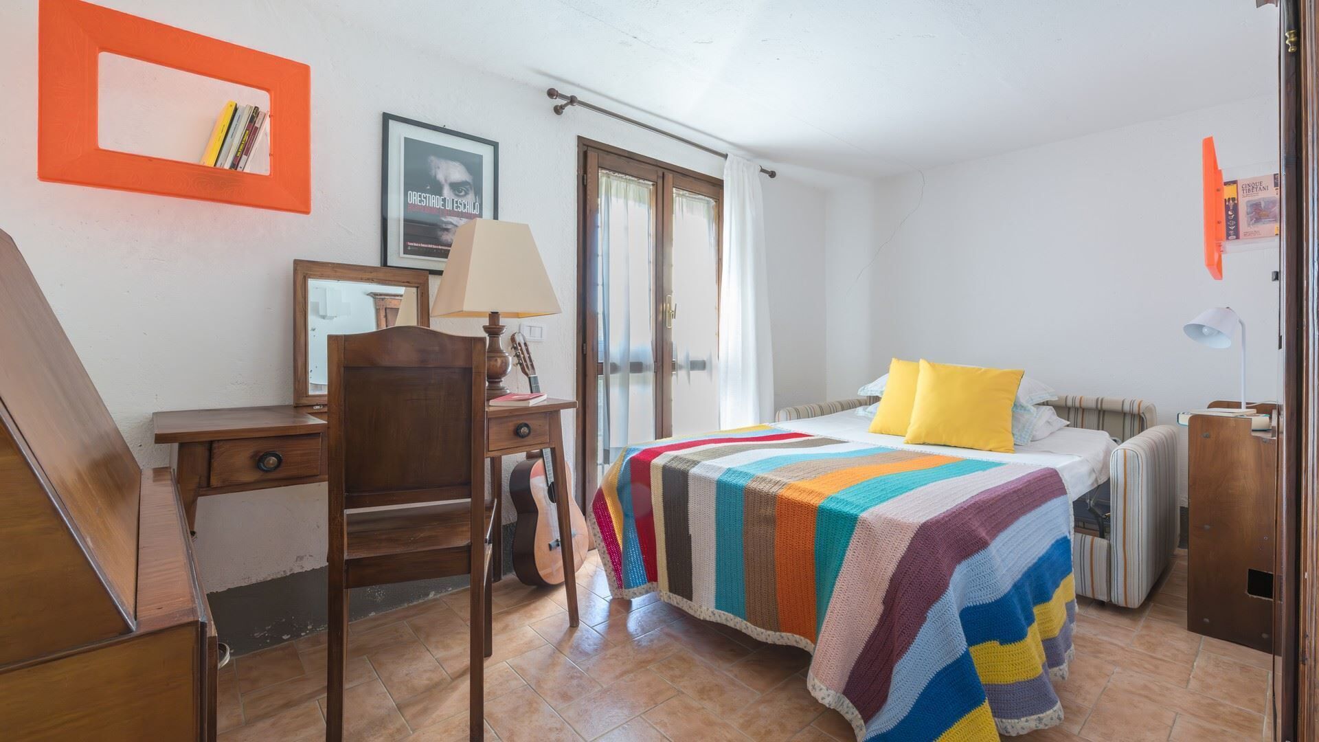 Une chambre avec un lit, un bureau, une chaise, une guitare et une fenêtre.