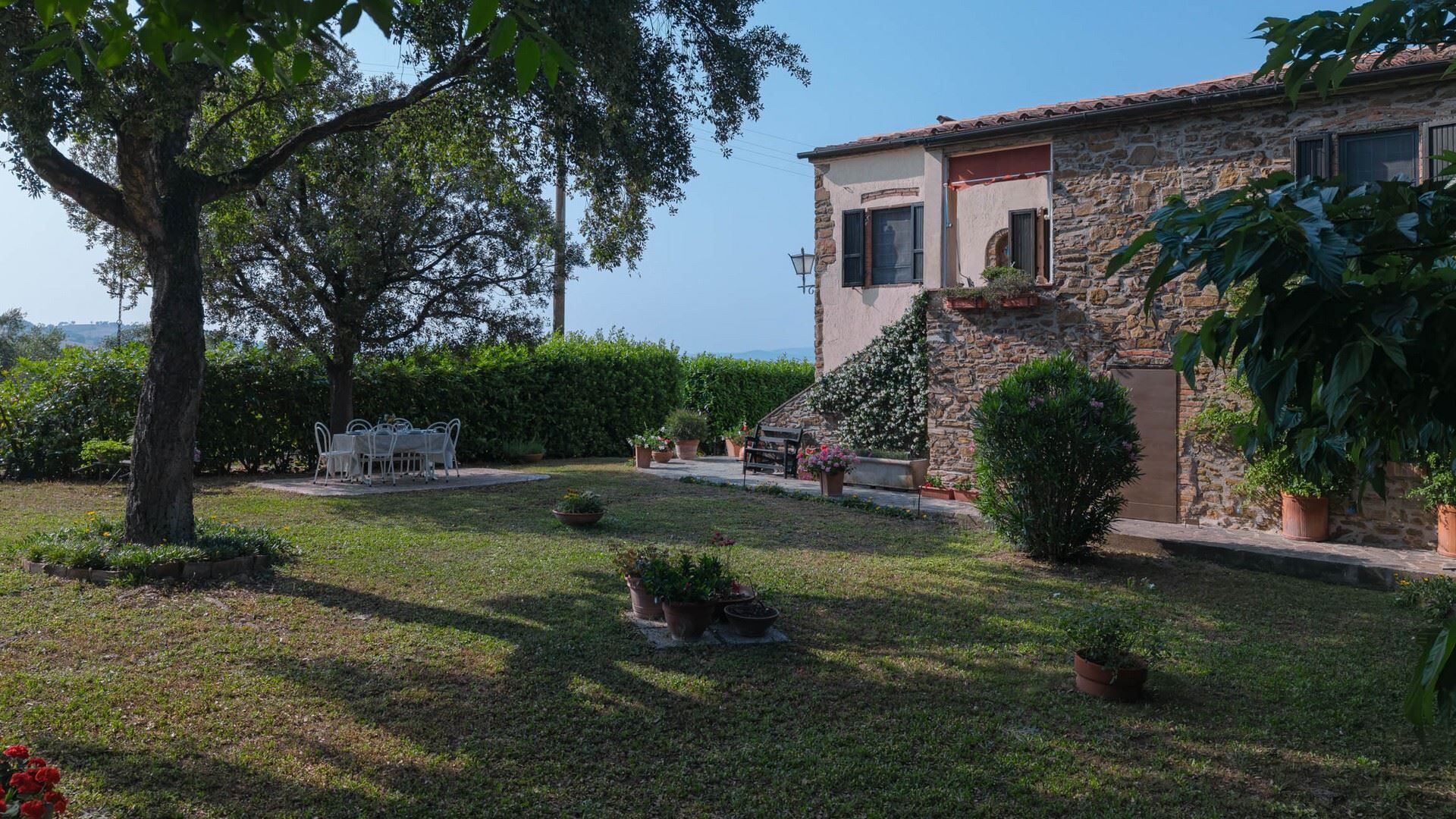 A stone house with a garden, a dining table, and potted plants.