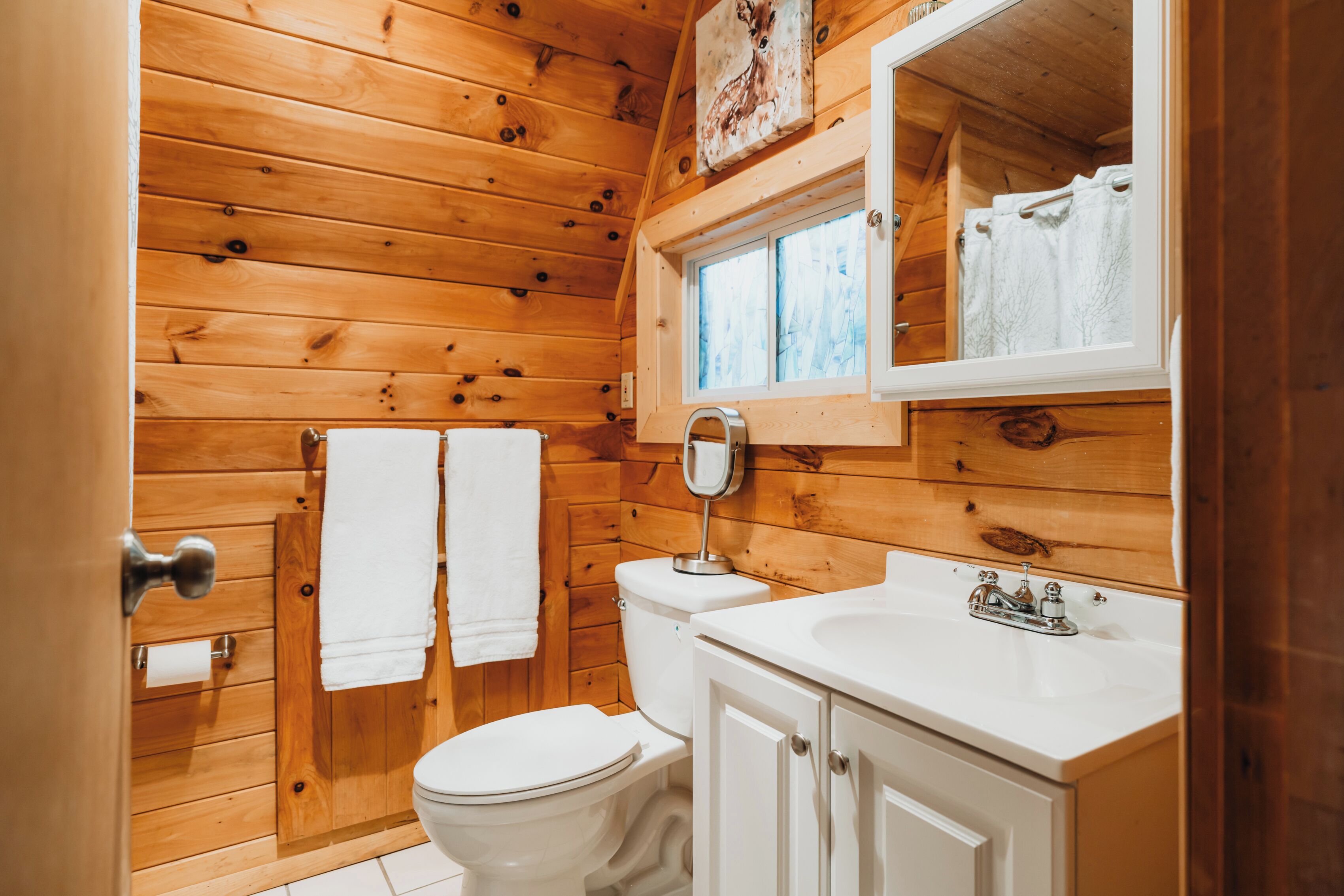 A wooden cabin bathroom with a toilet, sink, and mirror.