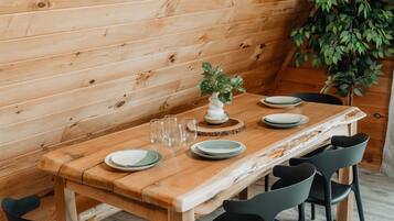 A wooden dining table with plates and glasses, surrounded by black chairs, in a room with wooden walls and a plant.