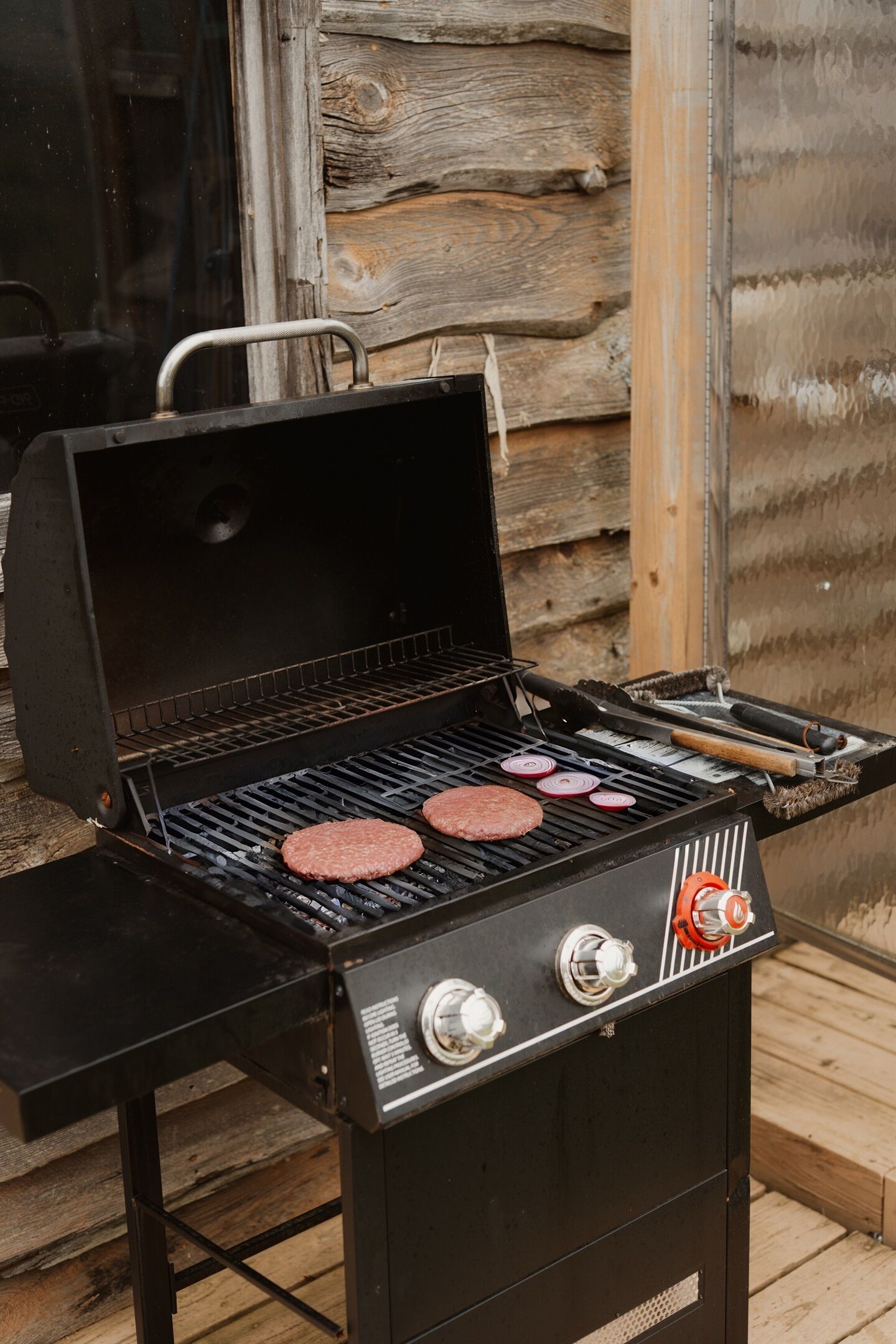 A barbecue grill with two burgers cooking, set against a wooden backdrop.