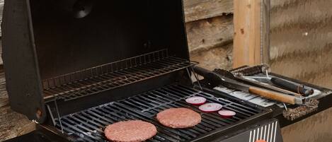 A barbecue grill with two burgers cooking, set against a wooden backdrop.