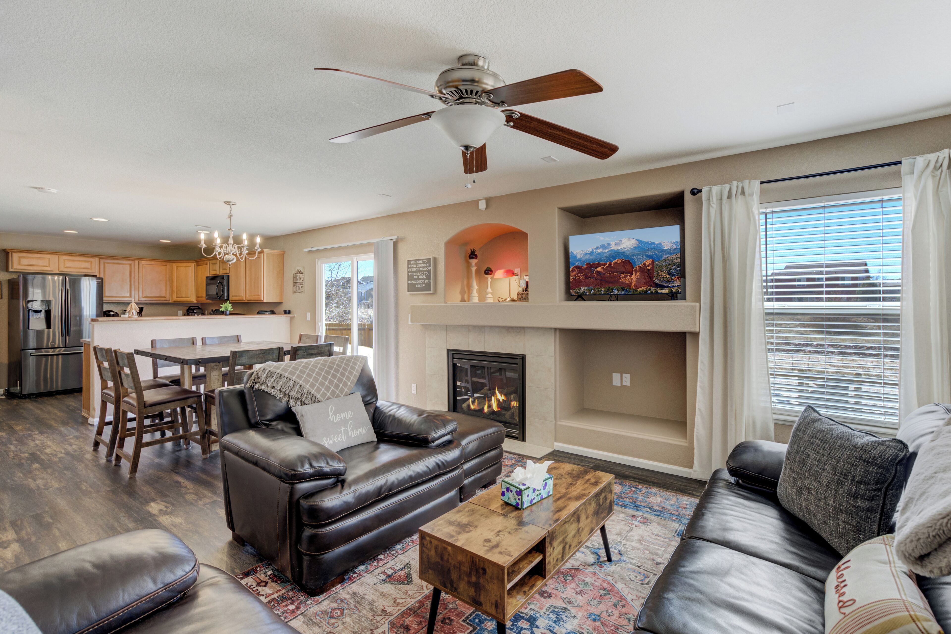 A spacious living room with a fireplace, leather sofas, a coffee table, and a dining area with wooden chairs and a kitchen in the background.