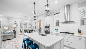 A modern kitchen with white cabinetry, a central island with stools, stainless steel appliances, and pendant lighting.