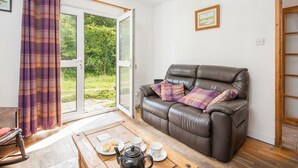 A cozy living room with a leather sofa, plaid cushions, a wooden coffee table with a teapot, cups, and a plate of cookies. - Cwmtawel, Holiday Cottage Ceibwr Bay, Sleeps 4, 3 bedrooms,  bathrooms (Cardigan)