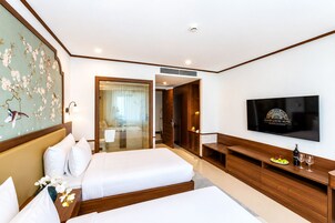 Habitación de hotel con cama, televisión, escritorio y baño visible a través de una puerta de cristal.