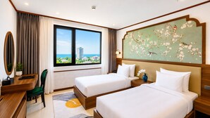 Habitación de hotel con dos camas, un escritorio, una silla, un ventanal con vistas y un adorno en la pared.