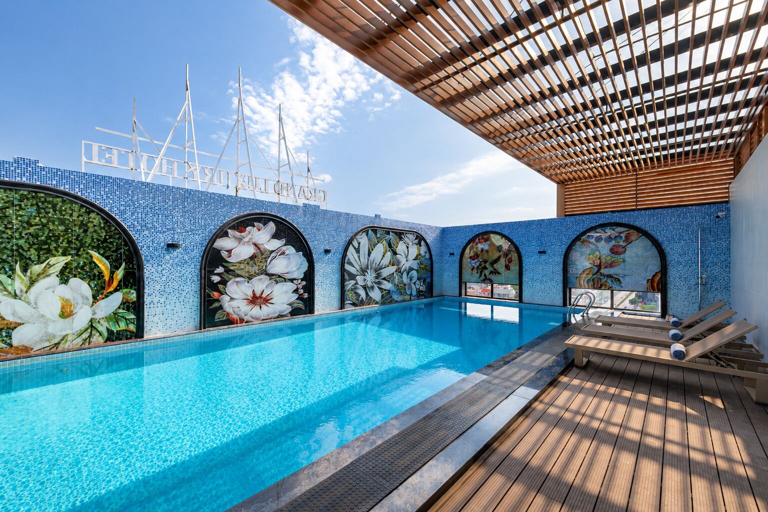 A pool area with a clear blue pool, wooden deck, and decorative floral tiles.