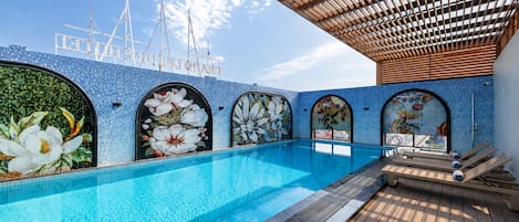 A pool area with a clear blue pool, wooden deck, and decorative floral tiles.
