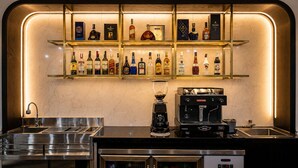 Una zona de bar con estantes llenos de botellas de licores, una máquina de café y un lavamanos.