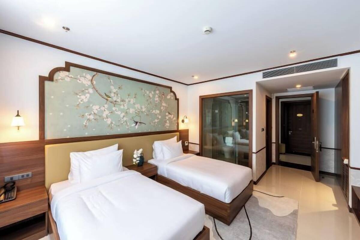A hotel room with two beds, a large floral artwork on the wall, a glass door leading to a balcony, and a modern design.