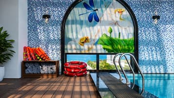 Un espace aménagé au bord de la piscine, avec une terrasse en bois, une bouée de sauvetage et une étagère contenant des serviettes.