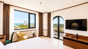 Habitación de hotel con una cama grande, televisión, vista al mar y balcón con plantas.