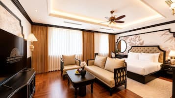 Habitación de hotel con cama, sofá, sillón, televisor y ventilador de techo.
