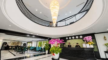 Un hall de hotel con una lámpara de araña imponente, una recepción y un área de descanso con sillas verdes.