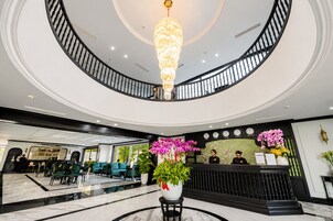 Un hall de hotel con una lámpara de araña imponente, una recepción y un área de descanso con sillas verdes.
