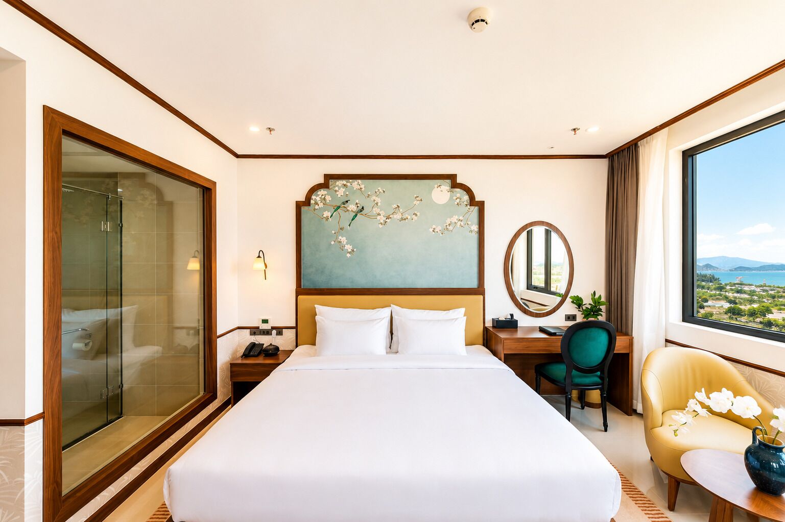 Une chambre d’hôtel avec un grand lit, un bureau avec une chaise, une douche en verre, un tableau au mur et une vue sur le paysage par la fenêtre.