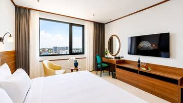 A hotel room with a bed, a desk with a chair, a television, and a large window with a view of buildings.