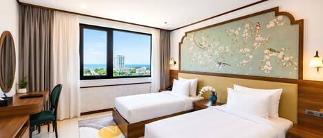 A hotel room with two beds, a desk, a chair, a large window with a view, and a decorative wall piece.