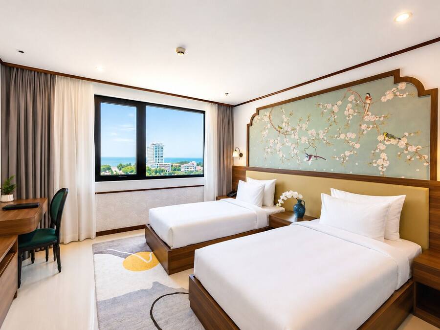 Une chambre d’hôtel avec deux lits, un bureau, une chaise, une grande fenêtre donnant sur un beau paysage et un élément décoratif mural.