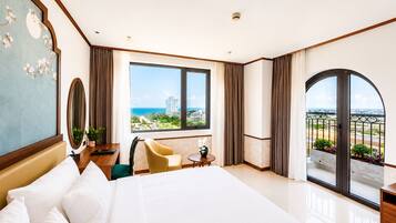 Habitación de hotel con una cama grande, un escritorio, una silla, una mesita y vistas a la ciudad y al océano.