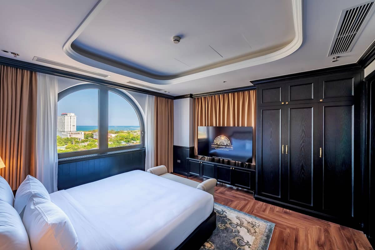 A hotel room with a large bed, a TV, a wardrobe, and a view of the city.