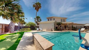 A swimming pool with a clear blue water, surrounded by a well-maintained lawn and palm trees. - Private Pool, Pet Friendly, 7 Minute Walk to the Beach (Port Aransas)