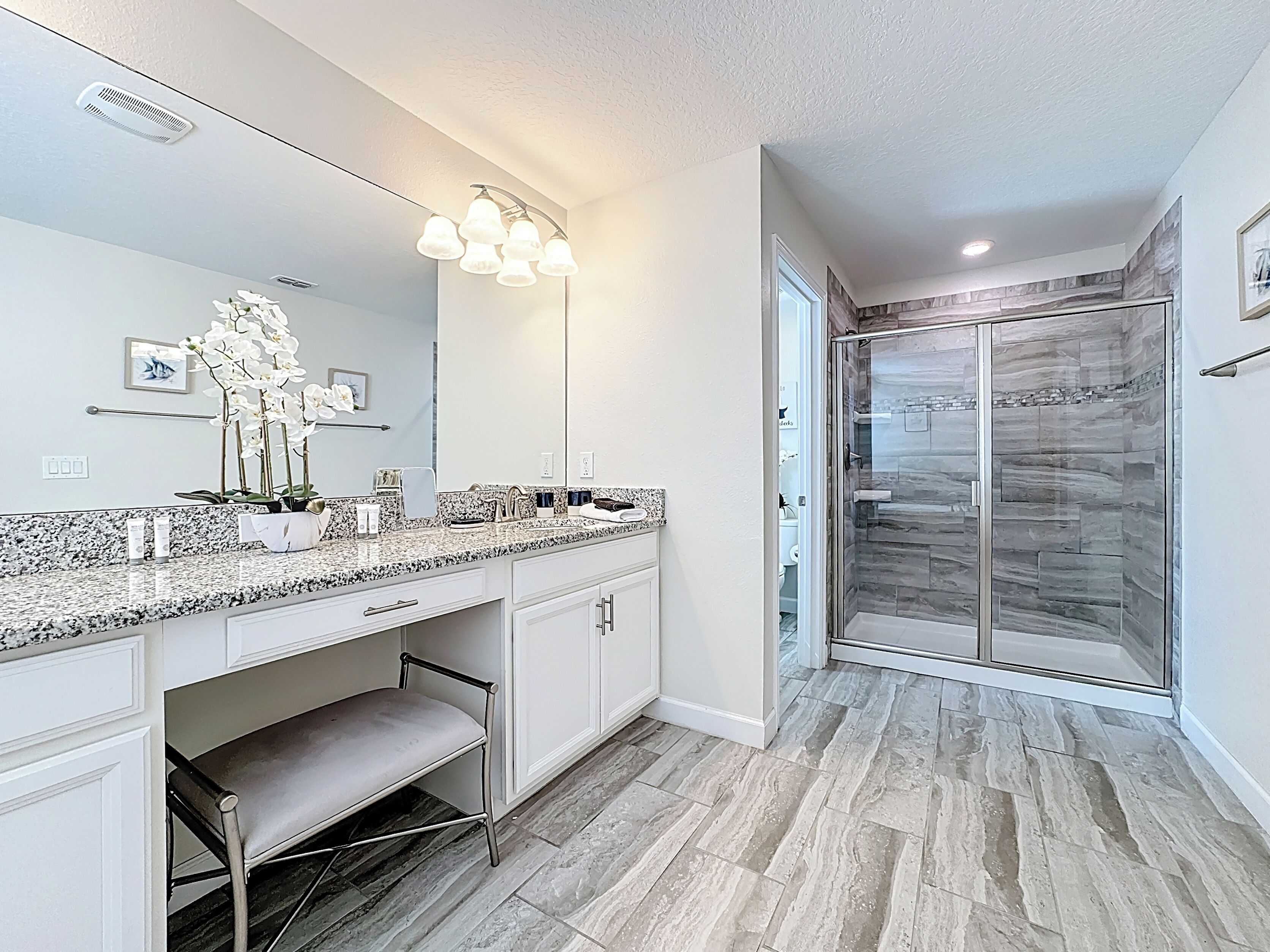 Une salle de bain moderne avec un comptoir en granit, un grand miroir, une douche à portes en verre et un banc.
