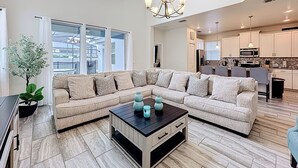 A spacious living room with a large sectional sofa, a coffee table, and a chandelier. - 🏝️ 5BR/5BA Home w/ Private Pool & Spa, Themed Kids’ Rooms & Resort Fun | Storey Lake Near Disney (Kissimmee)