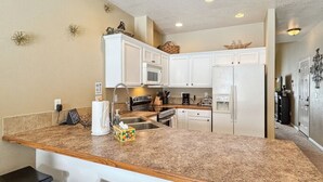 Una cocina con gabinetes blancos, encimera de granito y una isla integrada con taburetes de bar.