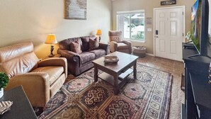 Una sala de estar con sofá, sillón, mesa de centro y televisor.