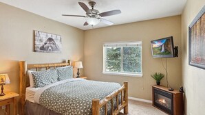 Un dormitorio con cama de madera, ventilador de techo, chimenea y ventana con vista a zonas verdes.