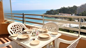 A balcony table set with plates, glasses, and cutlery, overlooking a beach and ocean.
