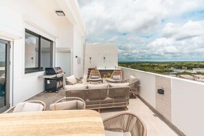Un balcon doté de meubles en osier, d’un barbecue et offrant une vue sur le paysage.