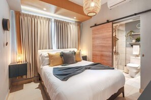 Une chambre moderne avec un grand lit, une table de chevet, un luminaire suspendu et une porte coulissante donnant accès à une salle de bain.