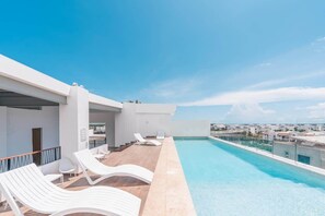 Une piscine sur le toit, dotée de chaises longues blanches et offrant une vue dégagée sur le paysage urbain.