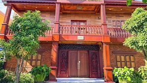 Une maison traditionnelle en bois, dotée d’un balcon, de grandes portes en bois et d’une entrée décorative.