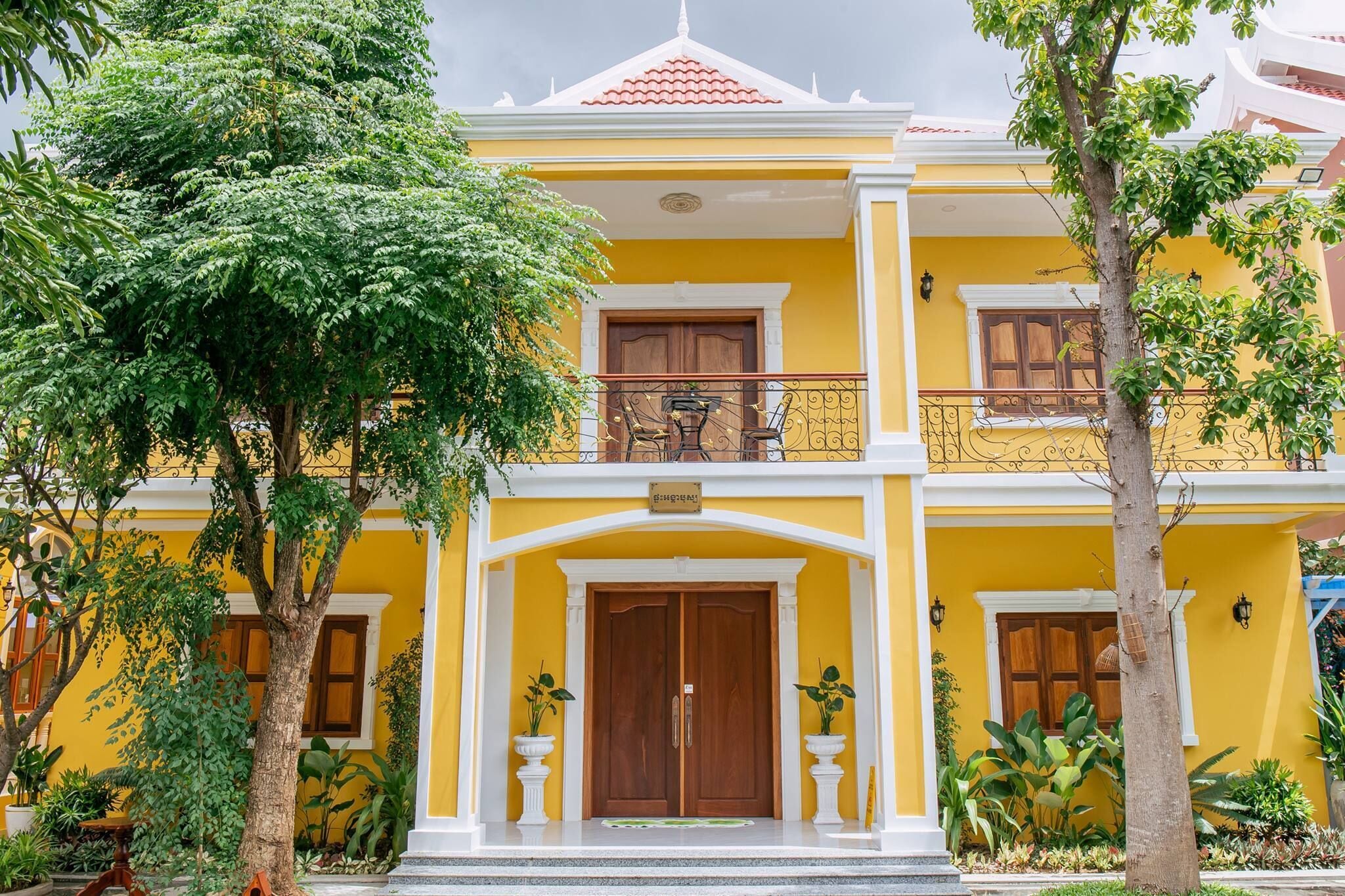 A two-story building with a yellow facade, a wooden door, and a balcony with a wrought iron railing.