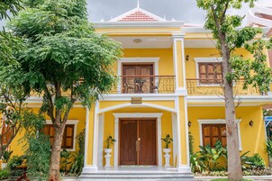 A two-story building with a yellow facade, a wooden door, and a balcony with a wrought iron railing.