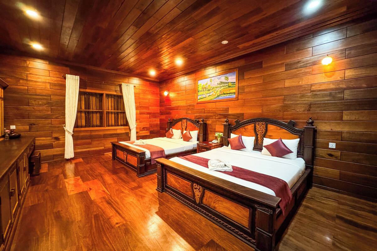 A wooden-themed room with two beds, a bench, and a bar area.